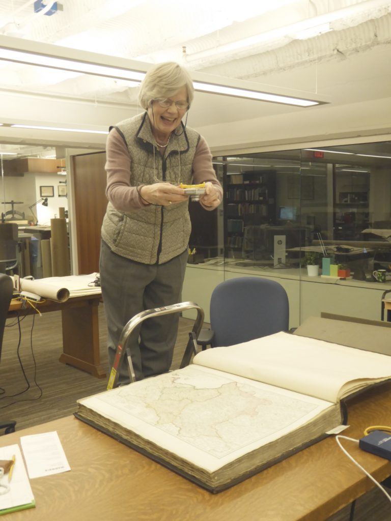 Mary Pedley stands on a stool to photograph an atlas